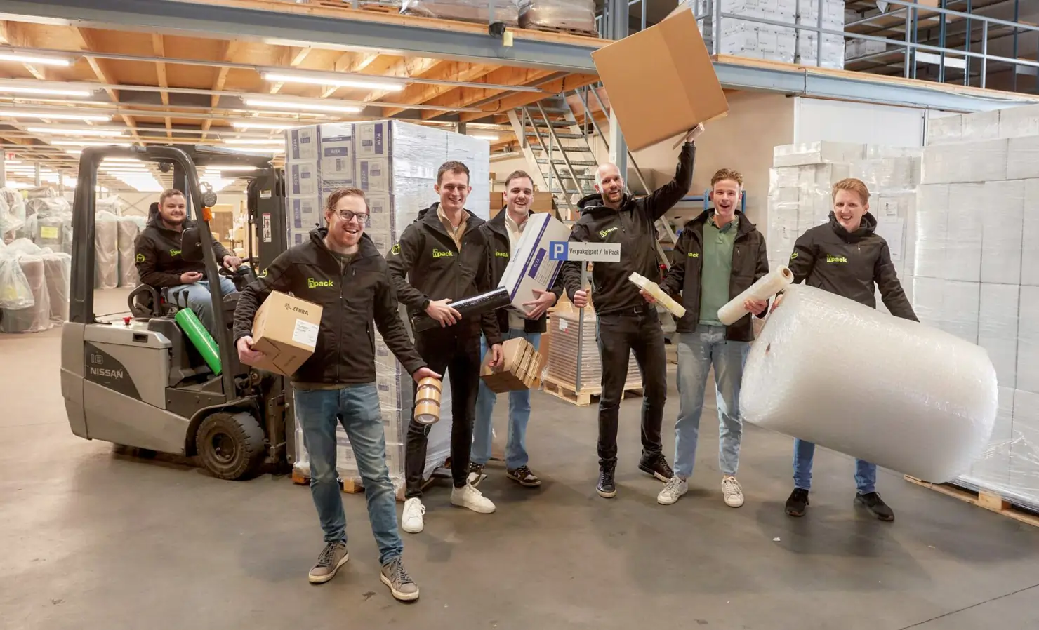 A bunch of the Verpakgigant team in their warehouse, some holding packaging, one on the forklift.